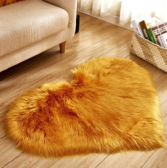 Fluffy gold silver heart-shaped plush carpet on wooden floor by beige sofa.