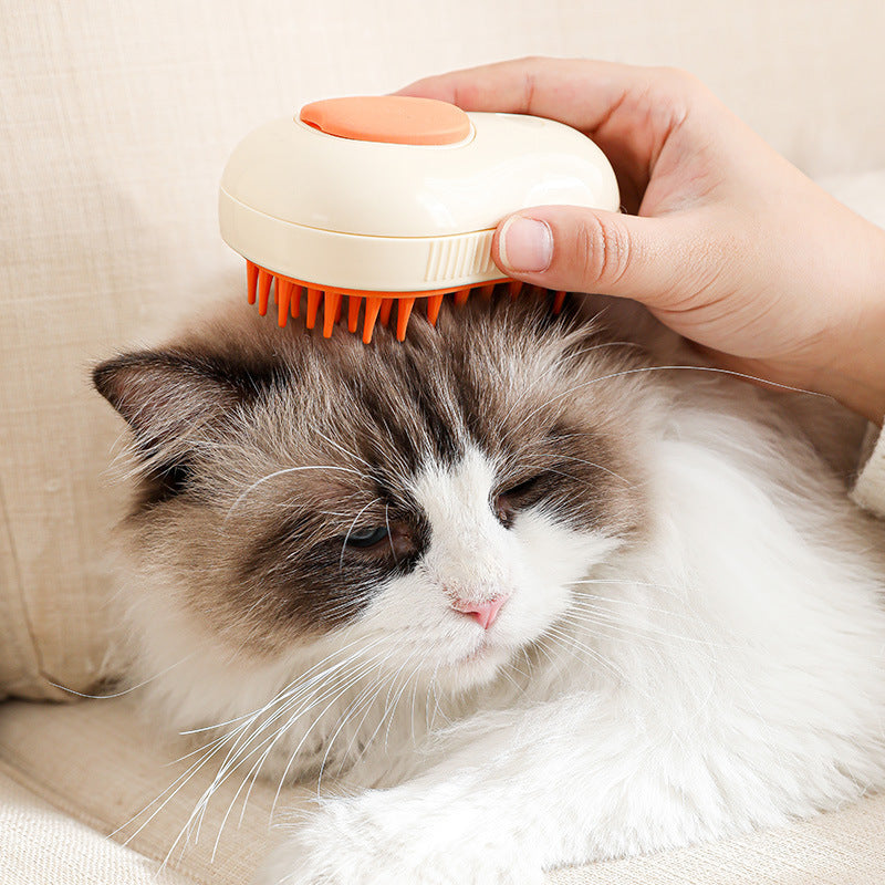 Cream white electric cat brush with orange bristles grooming a fluffy gray and white cat.