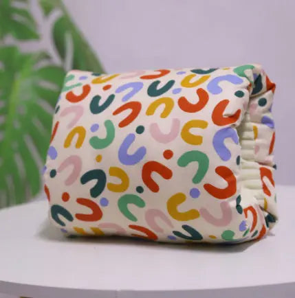 Beige cotton nursing arm pillow with colorful abstract horseshoe shapes pattern.