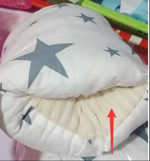 White nursing arm pillow with gray star pattern and beige ribbed fabric interior lining.