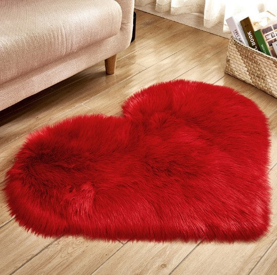 Fluffy red heart-shaped plush rug on wooden floor beside beige sofa.