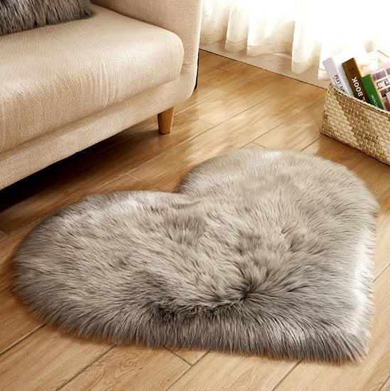 Fluffy heart-shaped carpet in soft gray with plush texture on wooden floor next to beige sofa.