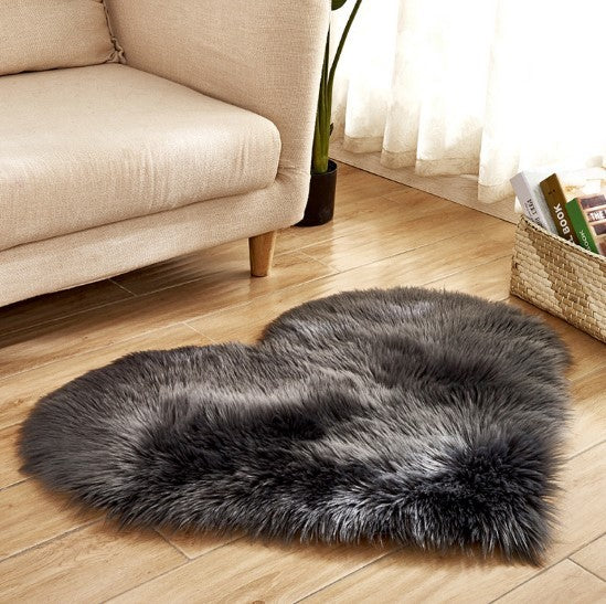 Dark grey plush heart-shaped carpet with fluffy texture on wooden floor near beige sofa.
