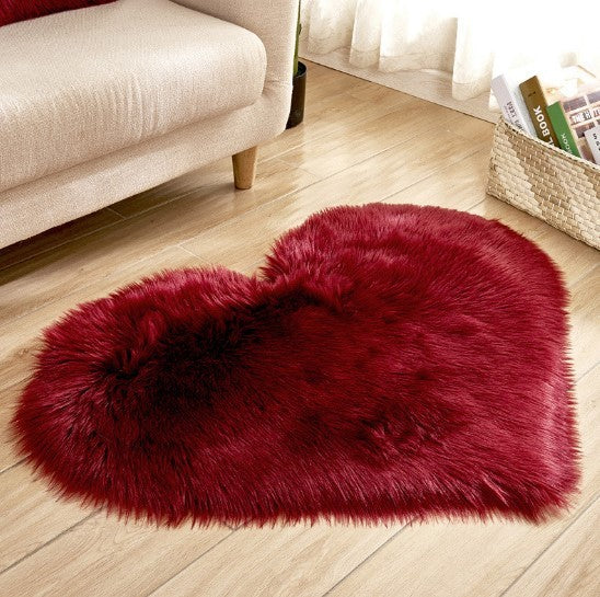 Fluffy deep red heart-shaped plush rug on wooden floor near beige sofa and basket.