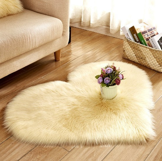 Heart-shaped fluffy rug in soft cream color on wooden floor with a small potted flower centerpiece.