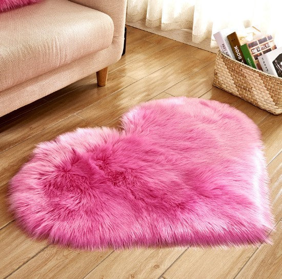 Fluffy heart-shaped pink plush carpet on wooden floor beside beige sofa and wicker basket.