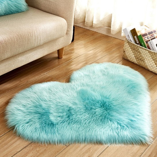 Fluffy light blue heart-shaped plush carpet on wooden floor beside beige sofa.
