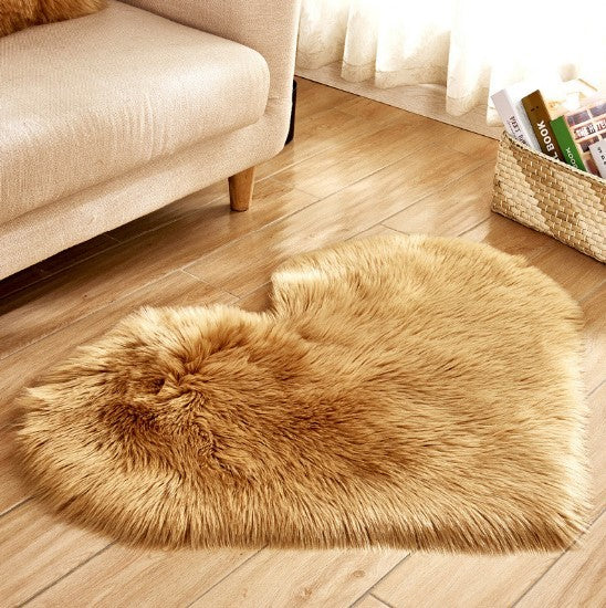 Plush fluffy heart-shaped carpet in warm camel color on wooden floor next to beige sofa.