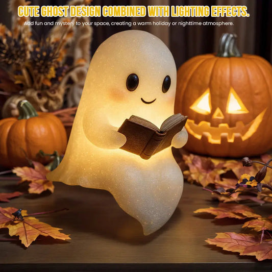Small white LED ghost night light holding a book, glowing warmly among autumn leaves and pumpkins.