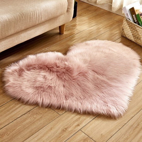 Fluffy heart-shaped plush rug in soft pink on wooden floor next to beige sofa.