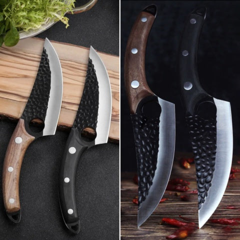 Two small butcher knives with hammered black steel blades and wooden and black handles side by side on a black surface with.