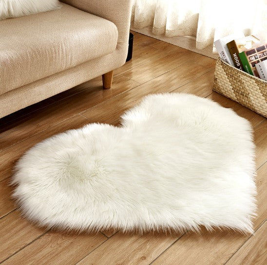 Fluffy white heart-shaped plush rug on wooden floor by beige sofa.