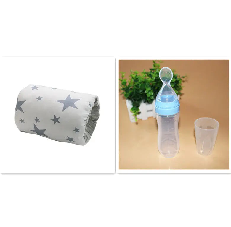 Beige nursing arm pillow with gray star pattern and clear baby bottle with blue lid and transparent cup on tan surface.